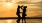 a man and woman holding hands and standing on a beach at sunset